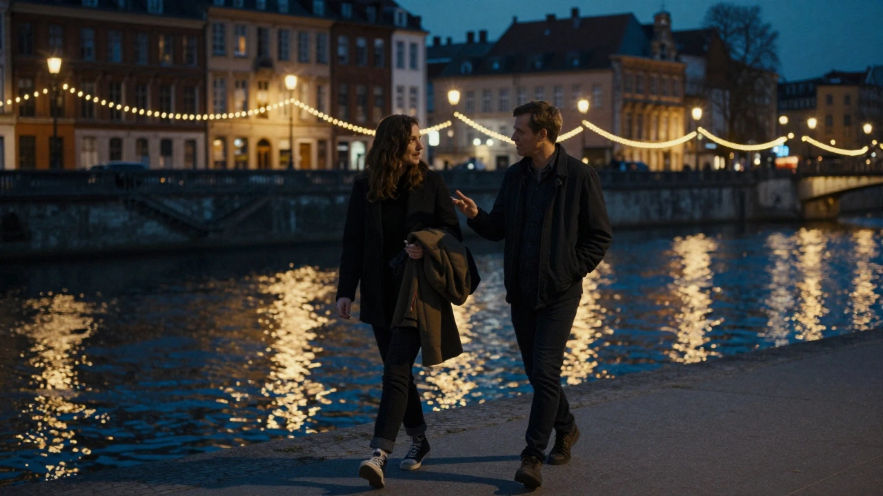 Two people walking peacefully along the Deûle River at night under string lights.